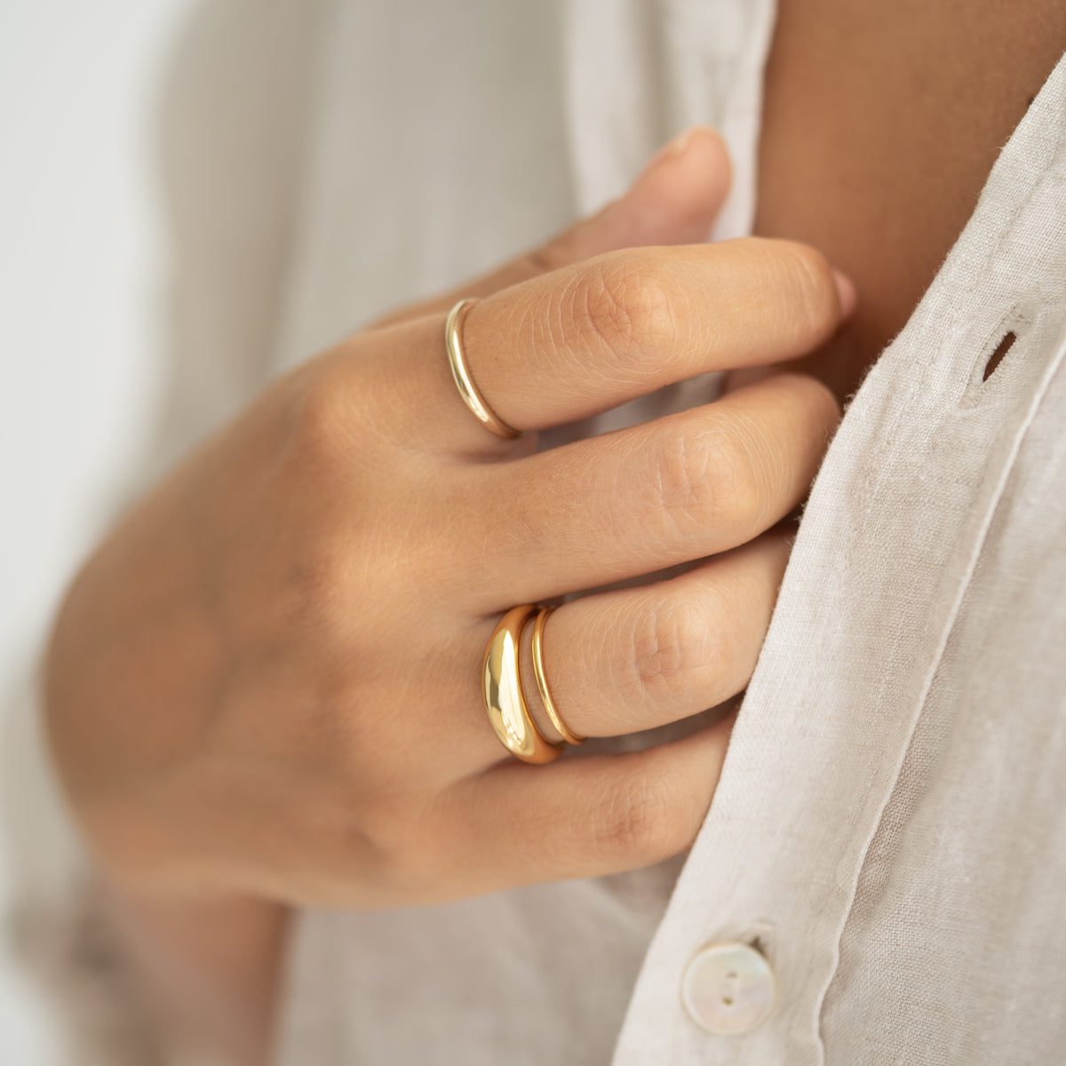 Close-up of hand wearing Thin Dome Ring 14k Gold - Mia paired with another gold ring on a white linen shirt