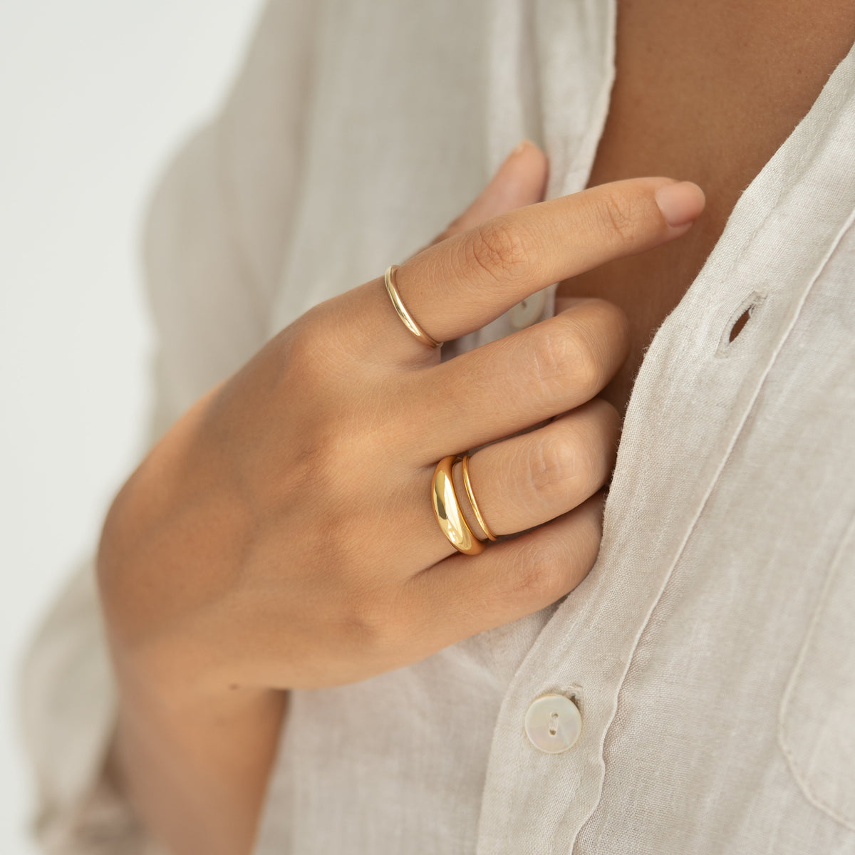Close-up of hand wearing Thin Dome Ring 14k Gold - Mia paired with other gold bands on a neutral linen shirt