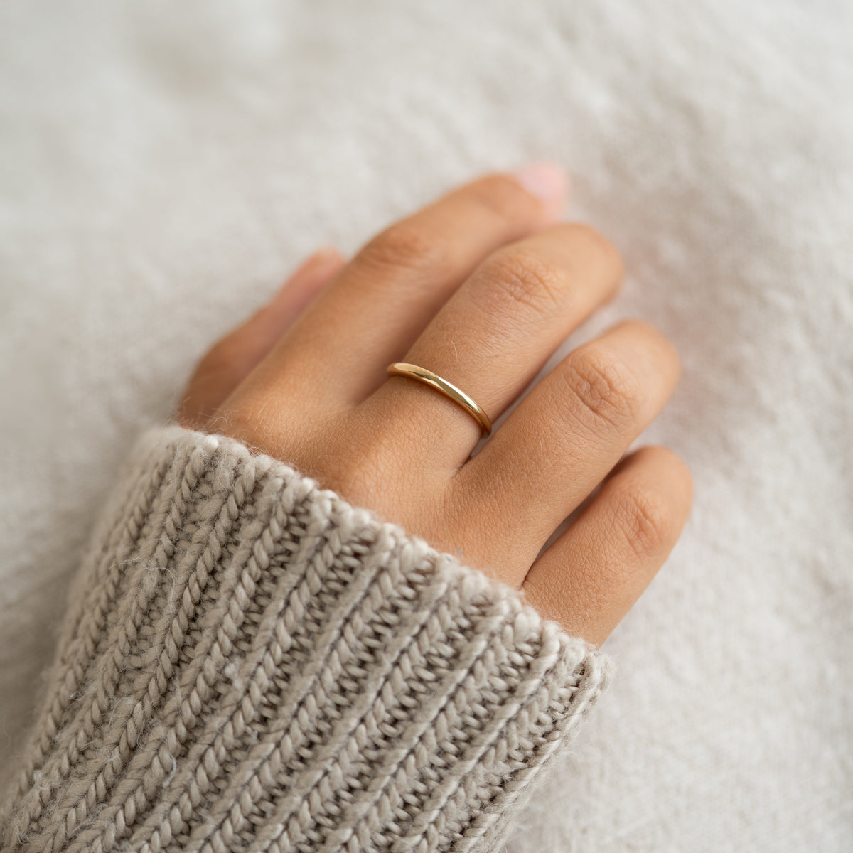 Close-up of a hand wearing the Thin Dome Ring 14k Gold - Mia on a cozy beige knitted sweater background