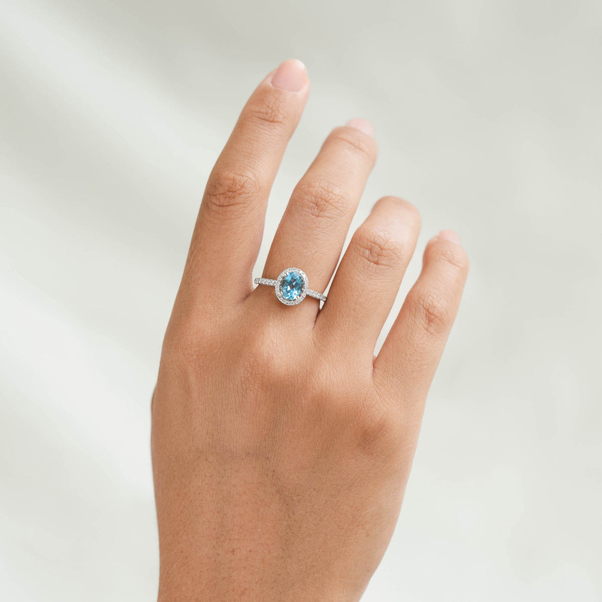 Oval Swiss Blue Topaz Halo Ring White Gold - Suna shown on hand with oval blue topaz and diamond halo on white gold band