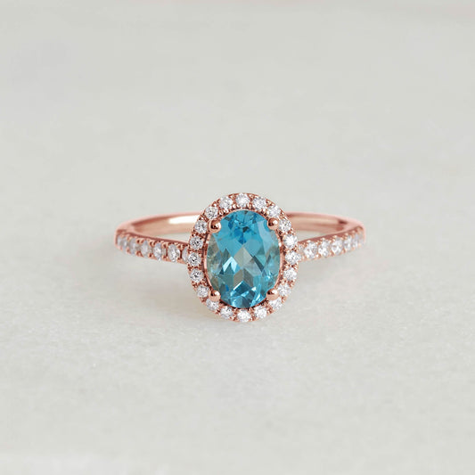 Oval Swiss Blue Topaz Halo Ring Rose Gold - Suna with pavé set diamonds and an oval blue topaz center on a neutral background