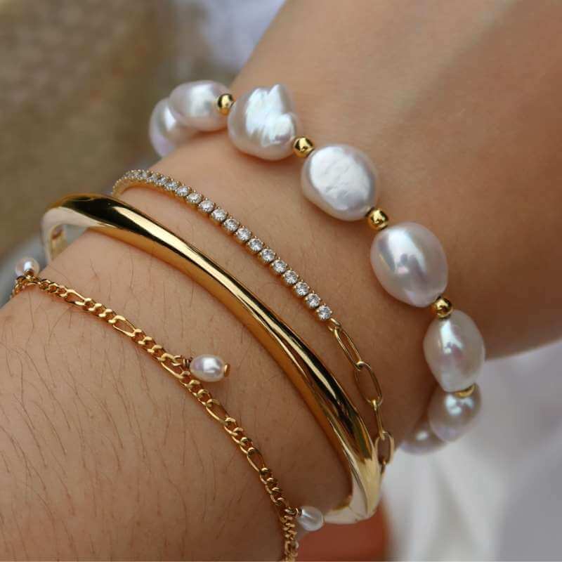 Close-up of a wrist adorned with layered gold bracelets, one with small pearls and another with a row of small clear stones on skin background