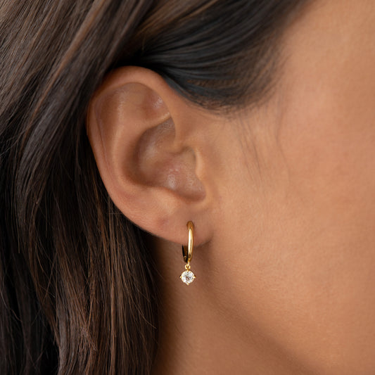 Close-up of a woman wearing April Birthstone Drop Huggie Earrings - White Topaz in gold vermeil on her ear
