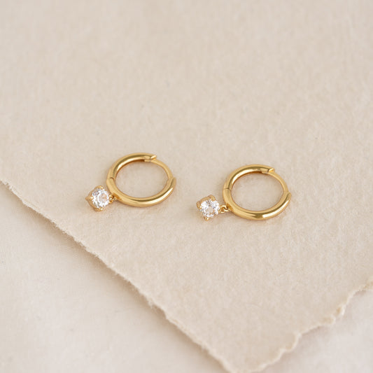 Close-up of April Birthstone Drop Huggie Earrings - White Topaz in gold vermeil on a neutral textured background