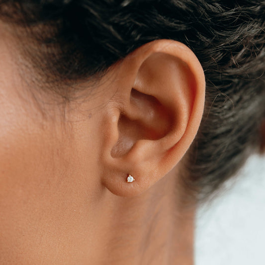 Close-up of an ear wearing 14k Yellow Gold Diamond Stud Earrings 2mm - Aria with a small round diamond in prong setting