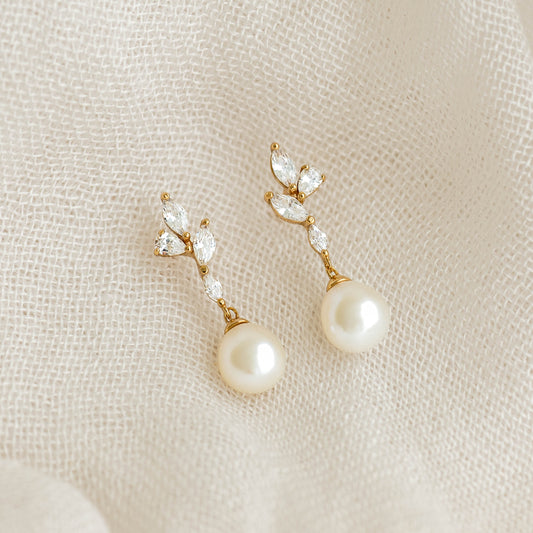 Close-up of Pearl Drop Earrings - Ariana featuring baroque pearls and cubic zirconia floral accents on beige fabric background