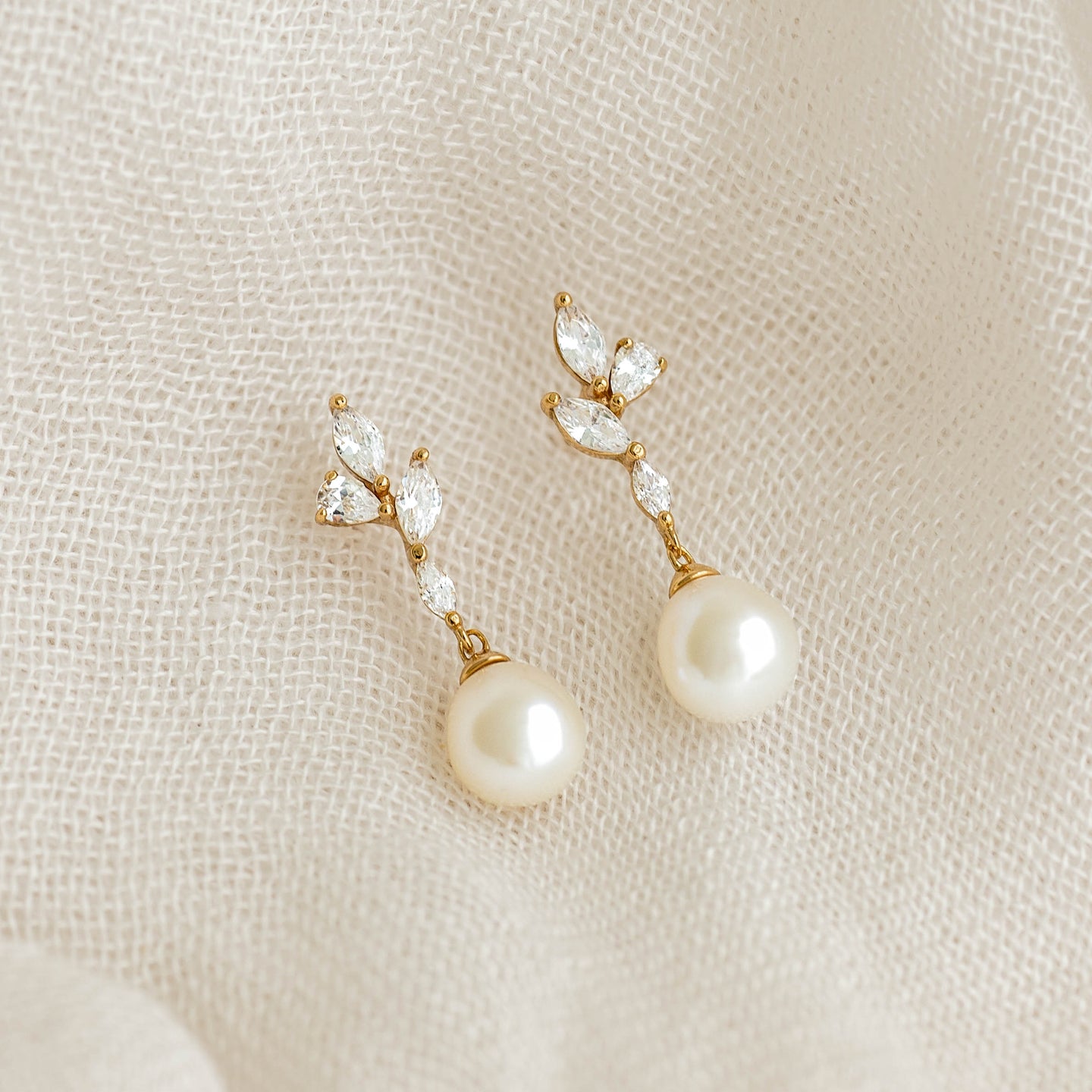 Close-up of Pearl Drop Earrings - Ariana featuring baroque pearls and cubic zirconia floral accents on beige fabric background