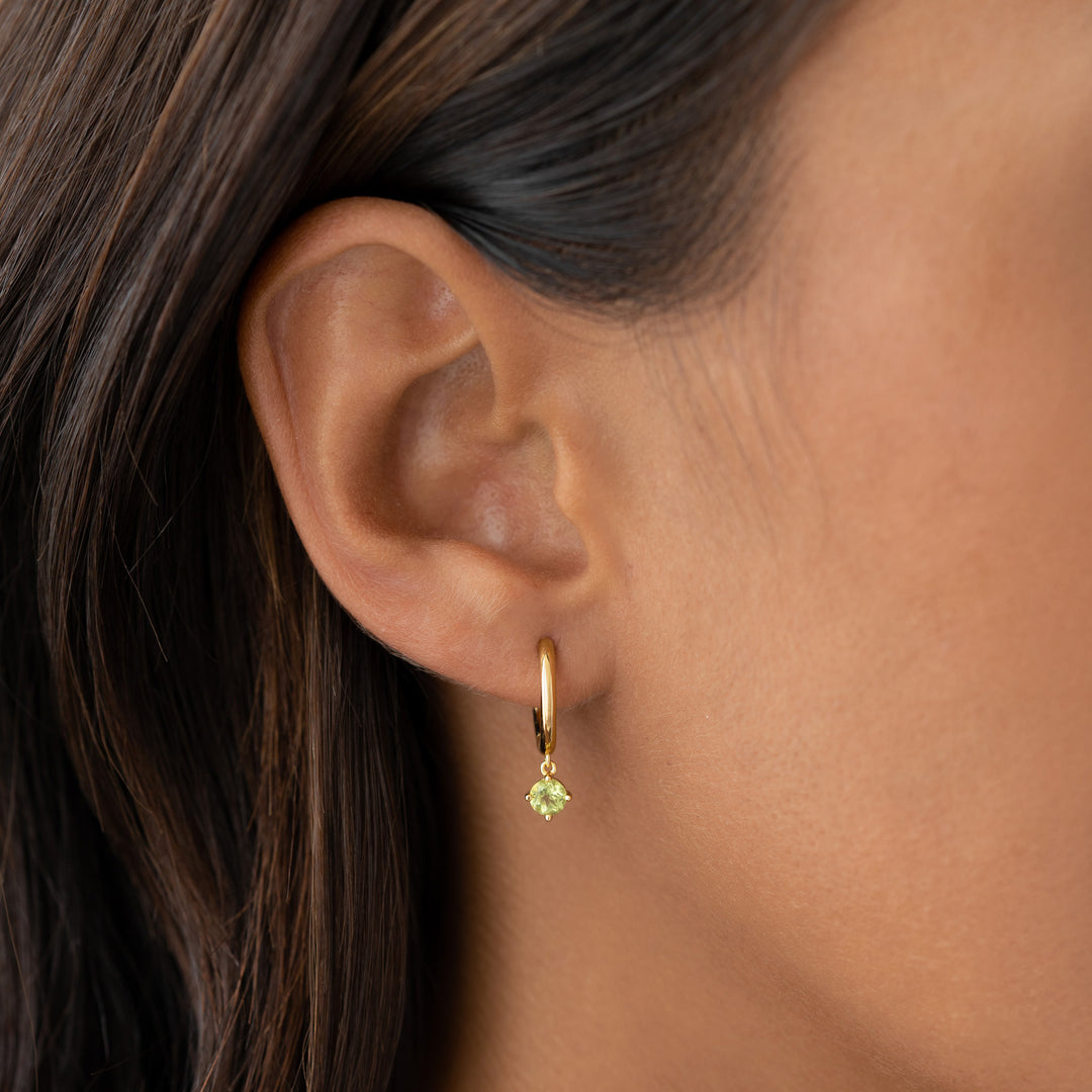 Close-up of ear wearing August Birthstone Drop Huggie Earrings - Peridot with gold vermeil and green gemstone drop
