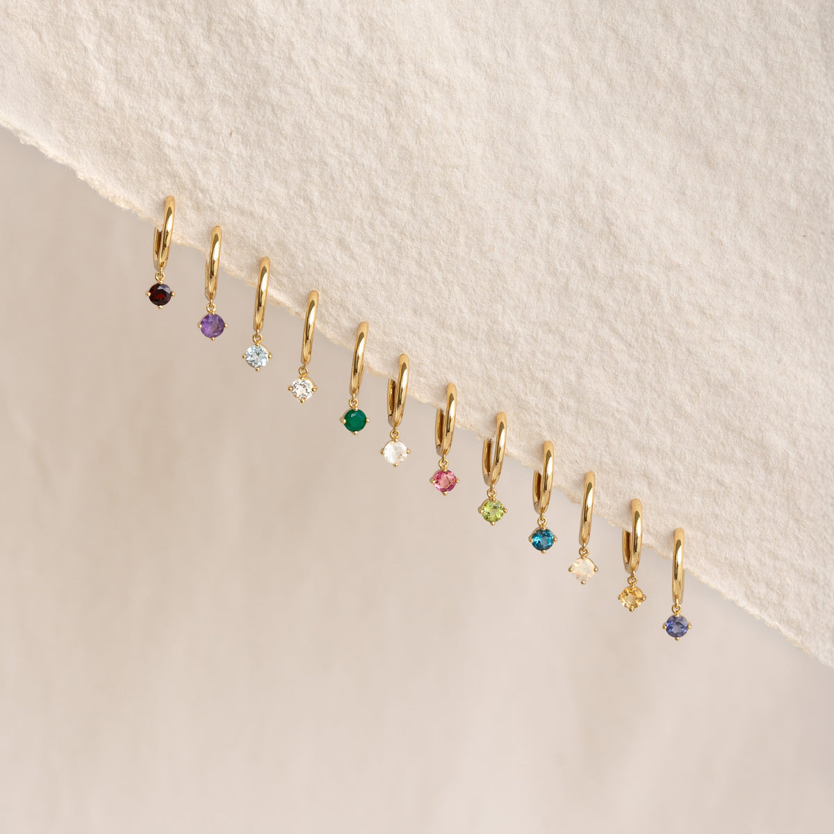 Row of gold vermeil huggie earrings with various gemstones featuring August Birthstone Drop Huggie Earrings - Peridot