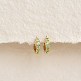 Close-up of August Birthstone Huggie Earrings - Olivine with green gemstones set in gold vermeil on a beige background