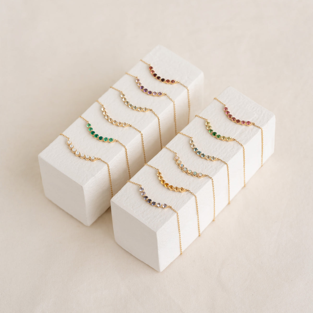 Collection of August Birthstone Necklace 14k Gold - Ombre Tsavorite with various multicolored gemstones displayed on white blocks