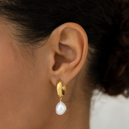 Close-up of an ear wearing Baroque Pearl Chunky Hoop Earrings - Meredith with gold vermeil and a freshwater baroque pearl pendant