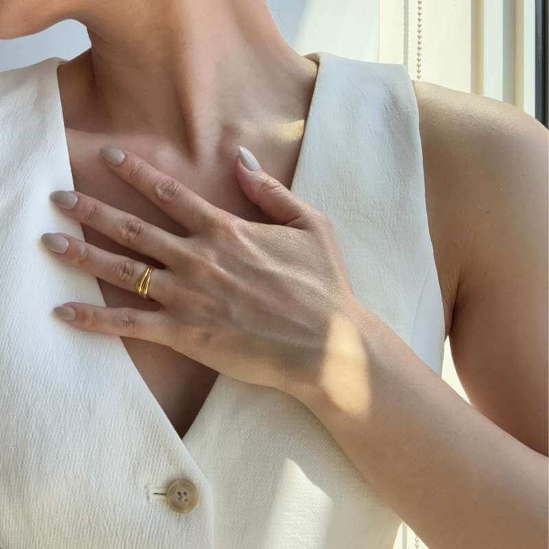 Close-up of a hand with beige polished nails resting on a white sleeveless textured fabric top near a window with soft natural light