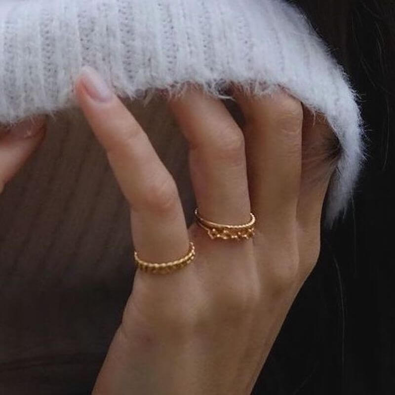 Close-up of a hand with two delicate gold rings partially covered by a white knit sleeve in soft lighting