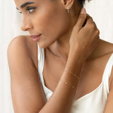 Close-up of a woman wearing the Bezel Set Diamond Bracelet 14k Gold - Vilda on her wrist with a white top and soft natural light