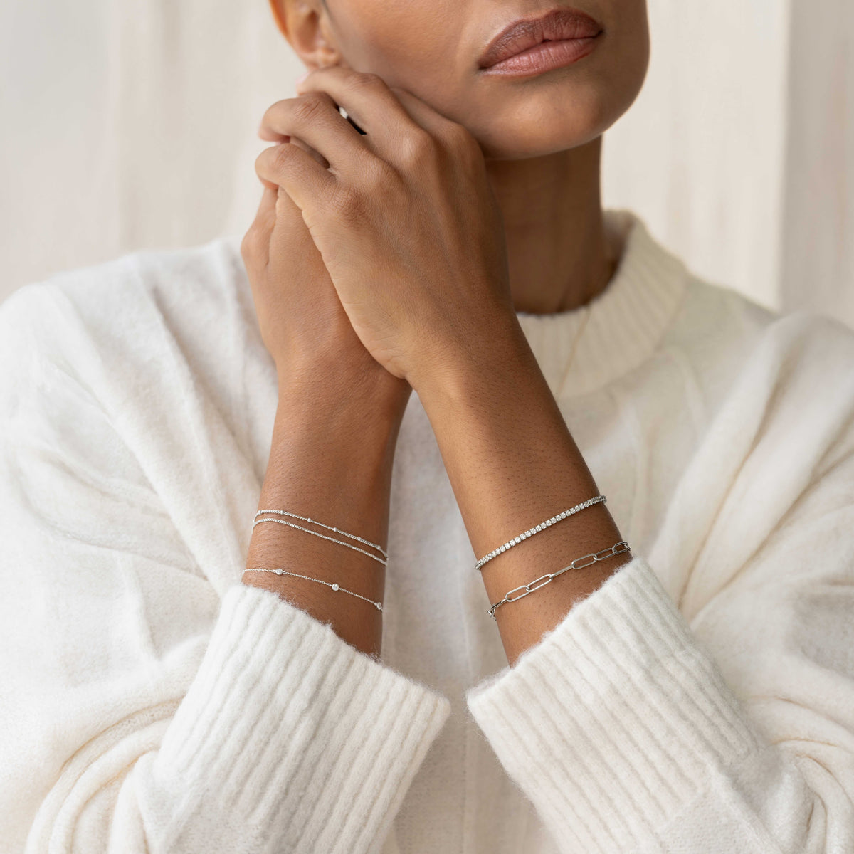 Close-up of a woman wearing Bezel Set Diamond Bracelet 14k White Gold - Vilda with layered delicate bracelets on white sweater