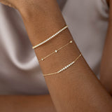 Close-up of wrist wearing Bezel Set Diamond Bracelet 14k Gold - Vilda with two delicate gold chain bracelets on neutral background