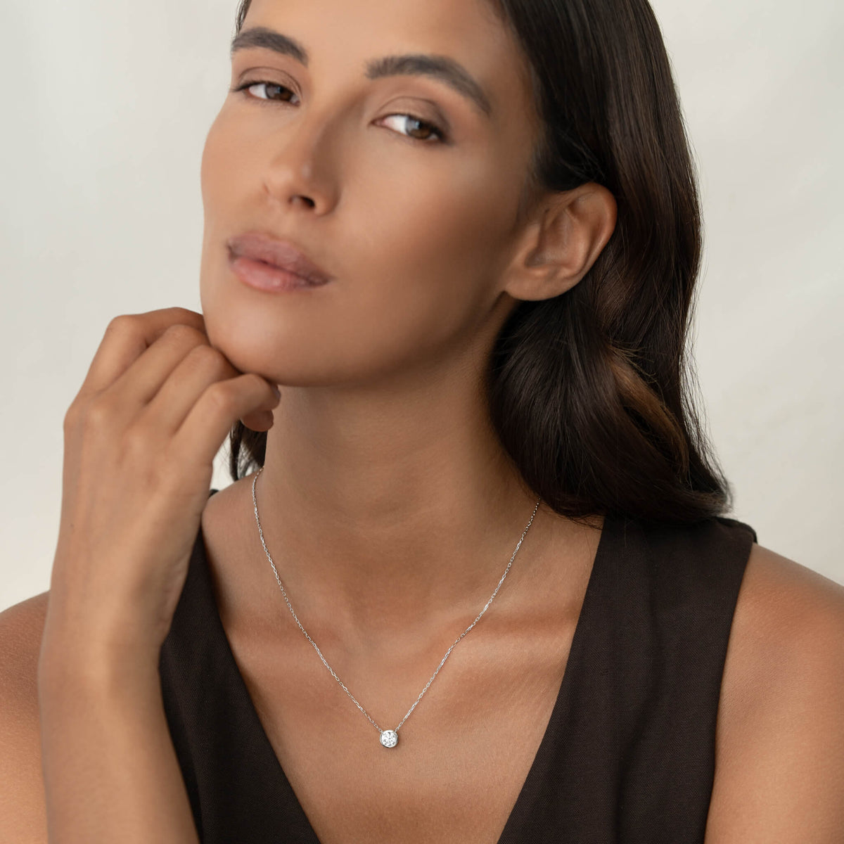 A close-up shot of a delicate White Gold necklace featuring a single, pear-shaped diamond pendant resting gracefully on a slender chain, worn against a person's neck.