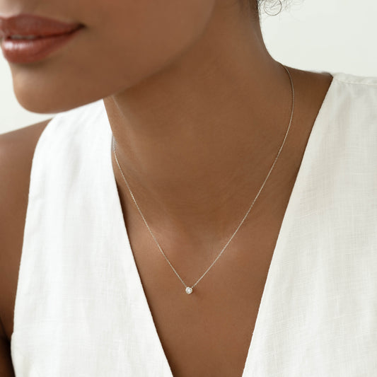 Close-up of a woman wearing a Bezel Set Diamond Necklace White Gold - Thais with a delicate 14k white gold chain and diamond pendant