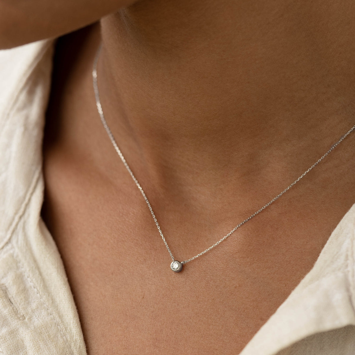Close-up of a woman wearing the Bezel Set Diamond Necklace White Gold - Thais with a simple white top