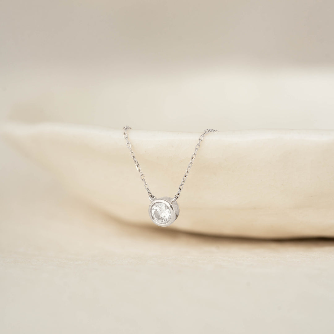 Bezel Set Diamond Necklace 4mm White Gold - Ulla resting on a neutral ceramic dish with soft natural lighting