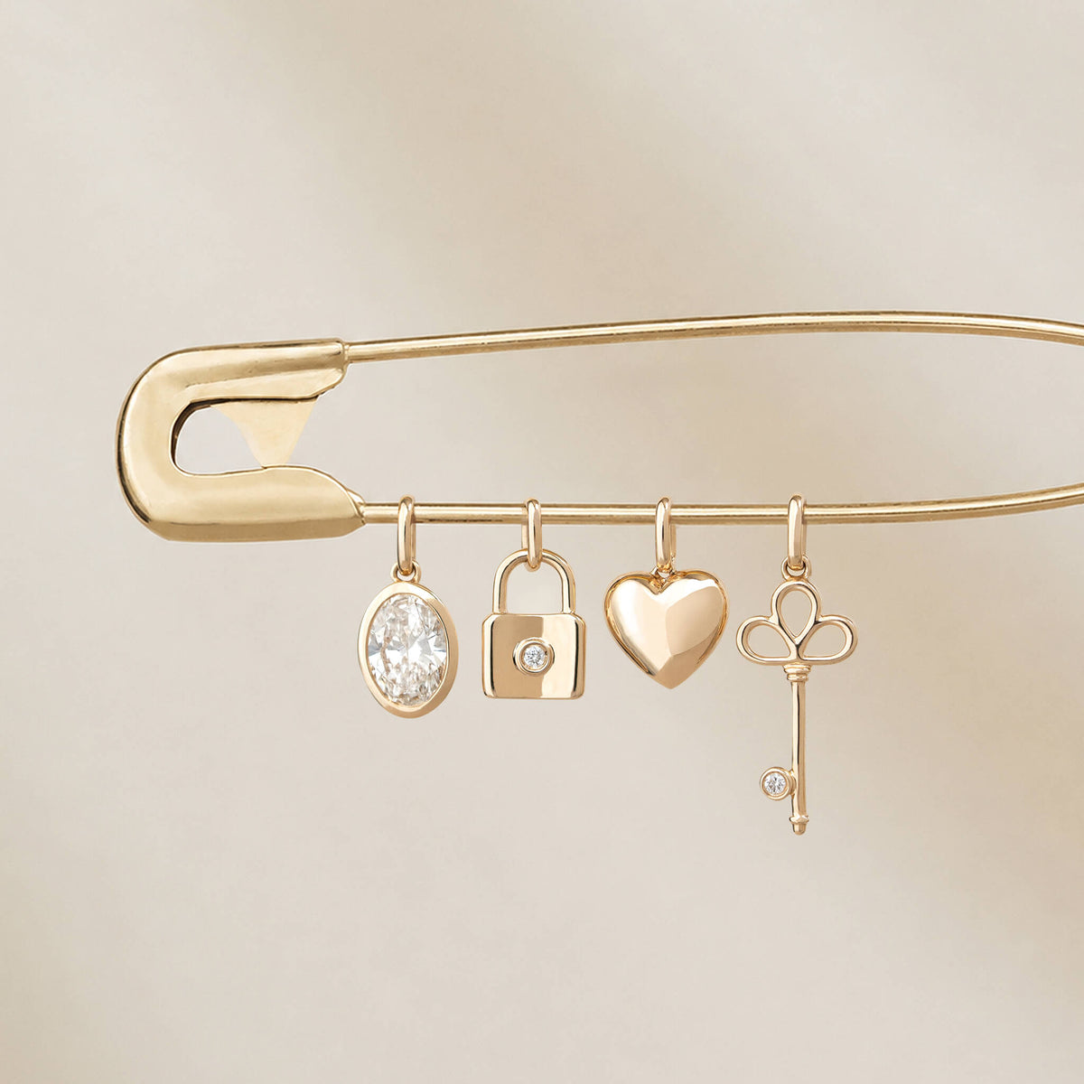 Yellow Gold safety pin featuring four hanging charms: an oval diamond charm, a padlock with a round diamond, a heart-shaped charm, and a key charm with a small diamond accent.