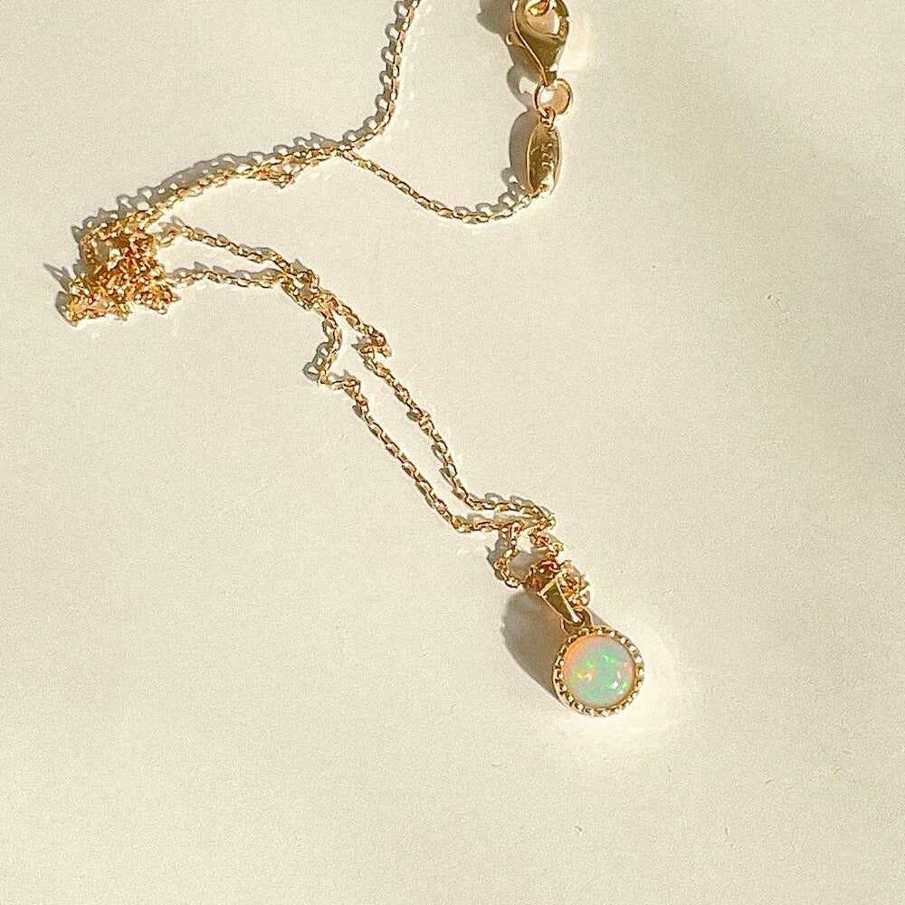 Delicate gold chain necklace featuring a small round opal pendant glowing softly against a neutral background