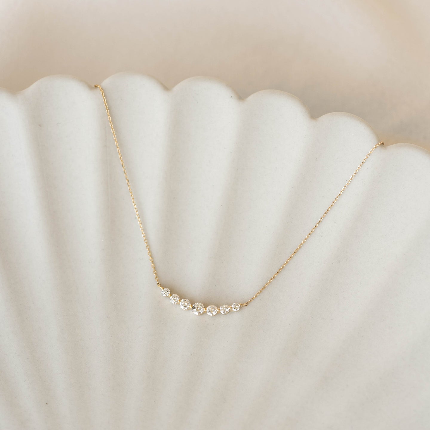 Graduated Diamond Necklace 14k Gold - Caterina with seven diamonds on a delicate curved gold chain on a soft background
