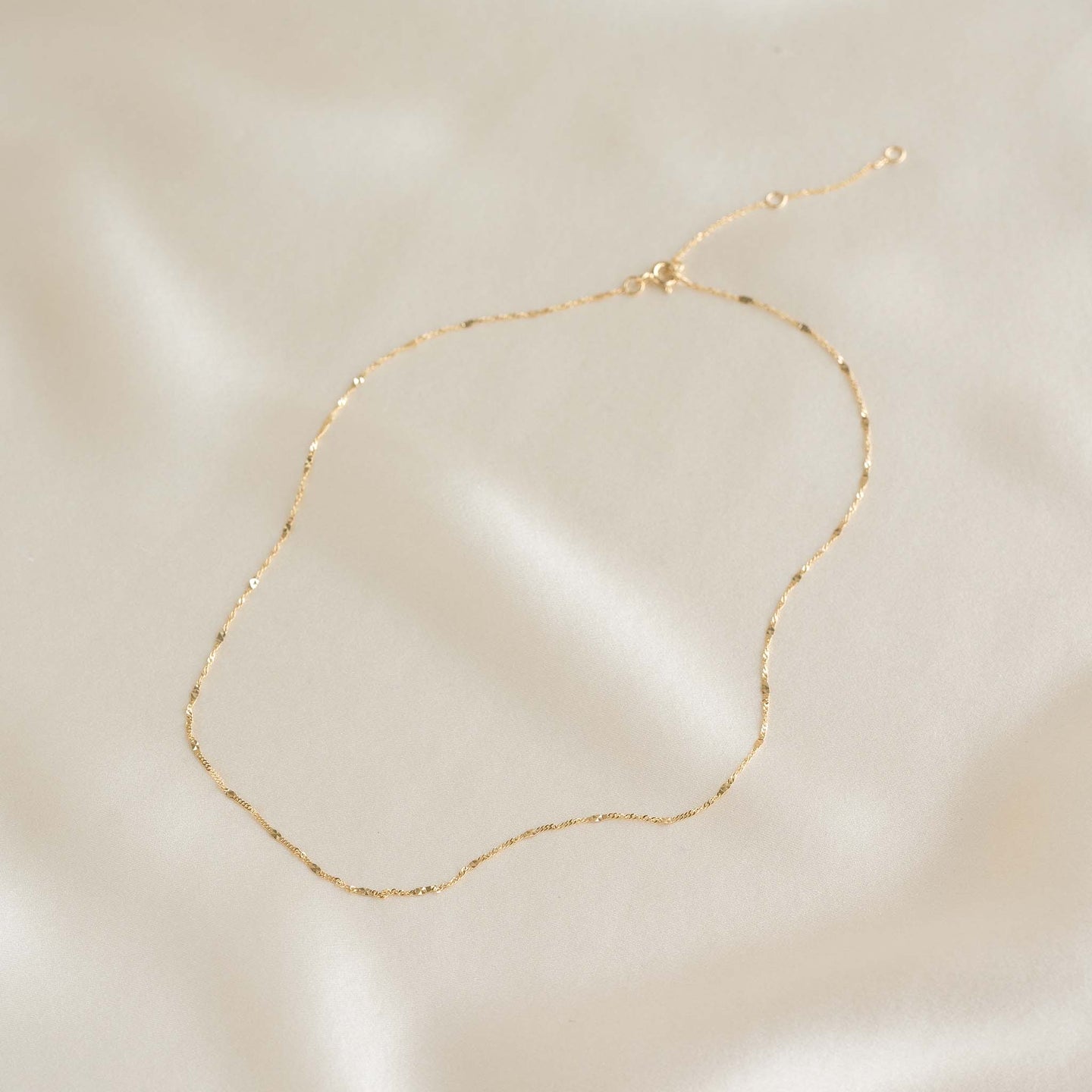 Shimmer Chain Necklace 14k Gold - Clara laid on soft beige fabric showing delicate mixed link design