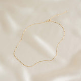 Shimmer Chain Necklace 14k Gold - Clara laid on soft beige fabric showing delicate mixed link design