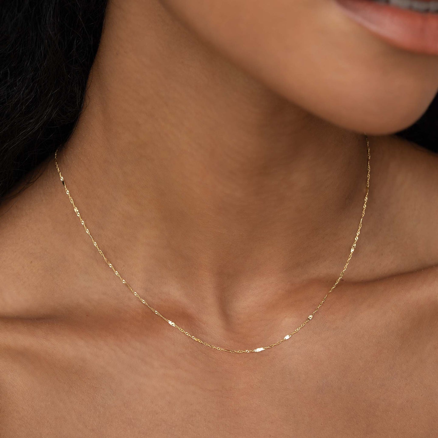 Close-up of a woman wearing the Shimmer Chain Necklace 14k Gold - Clara with a delicate yellow gold mixed link chain