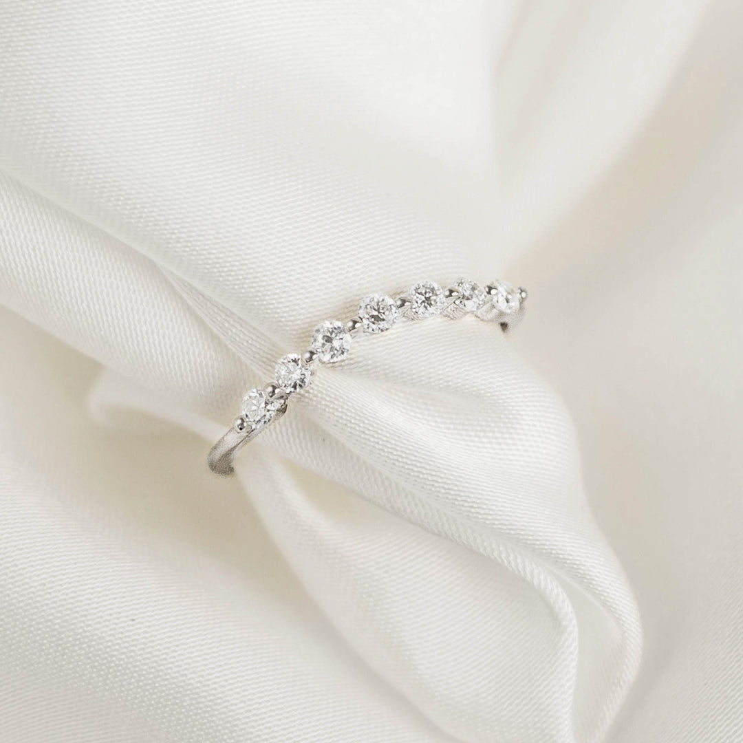 Close-up of Curved Diamond Ring White Gold - Isla featuring seven round diamonds on a sleek white gold band on white fabric