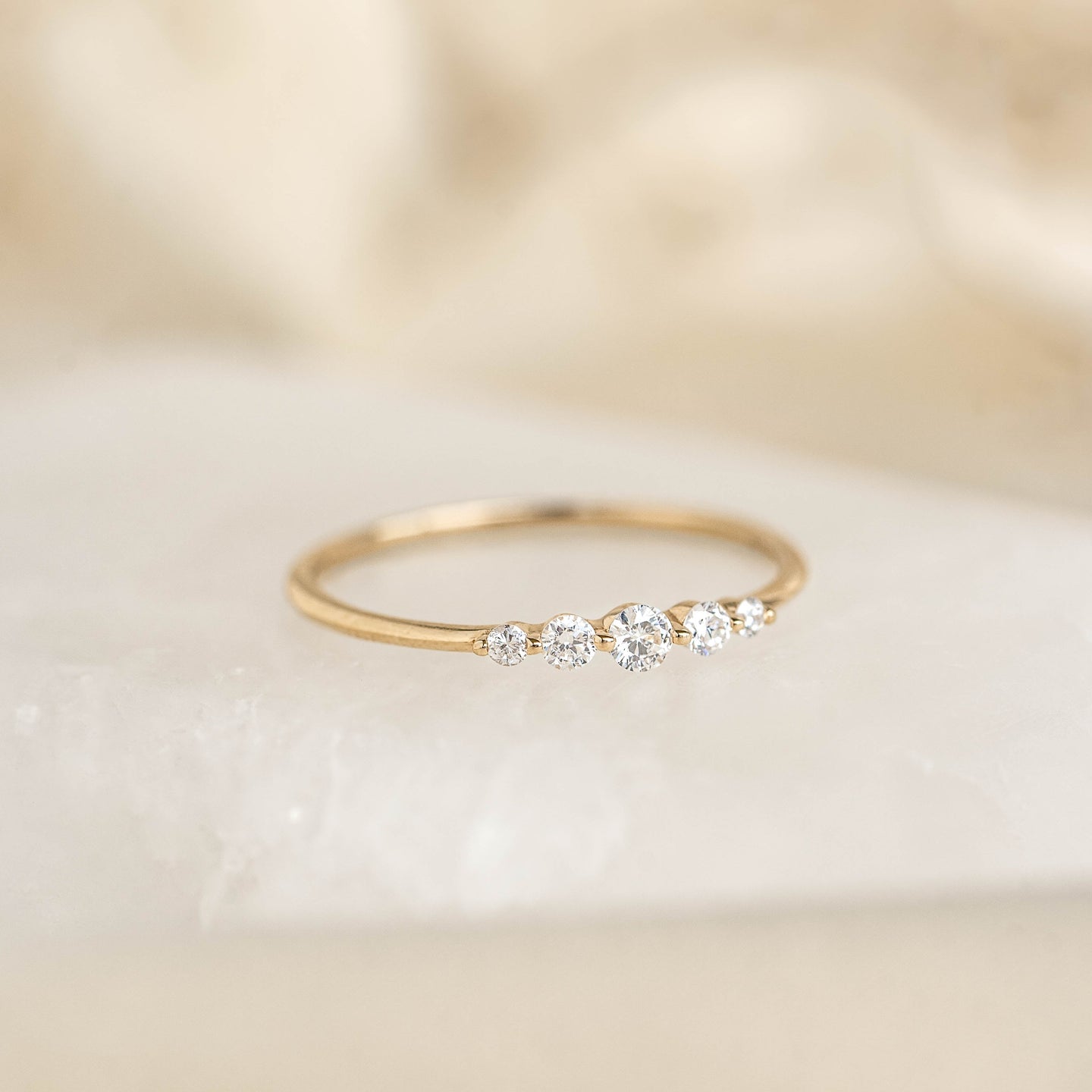 Close-up of Graduated Diamond Ring 14k Gold - Dahlia featuring five varying sized diamonds on a thin gold band