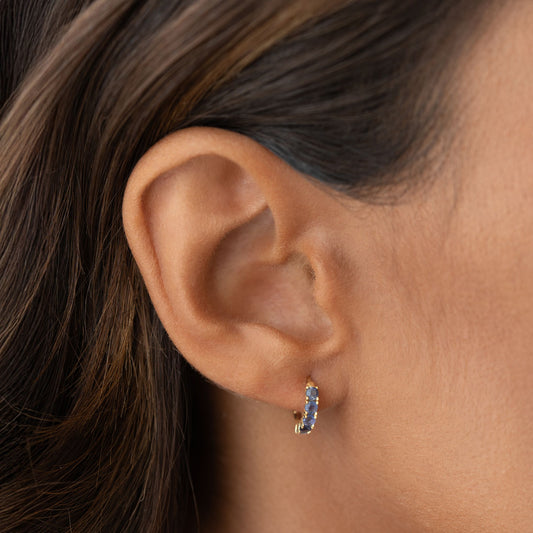 Close-up of ear wearing December Birthstone Huggie Earrings - Cordierite with blue stones set in gold vermeil