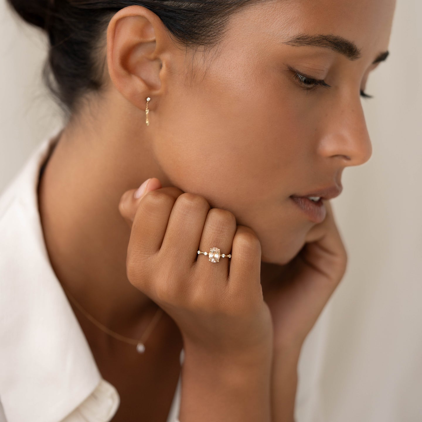 Woman wearing Oval Morganite and Diamond Ring 14k Gold - Demetria with subtle gold earrings and white shirt in soft light