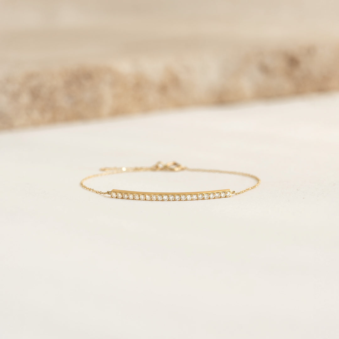 Close-up of Diamond Curved Bar Bracelet 14k Gold - Vivienne with 21 sparkling diamonds on a delicate gold chain on a light surface