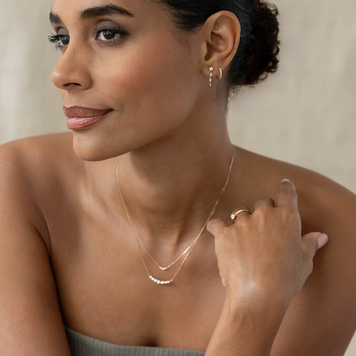 Woman wearing Diamond Drop Earrings 14k Gold - Helmi with matching gold necklace and ring against neutral background