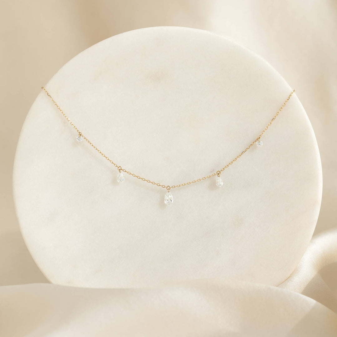 A delicate Gold necklace with small teardrop crystals draped gracefully on a round, white marble surface, set against a soft beige background.