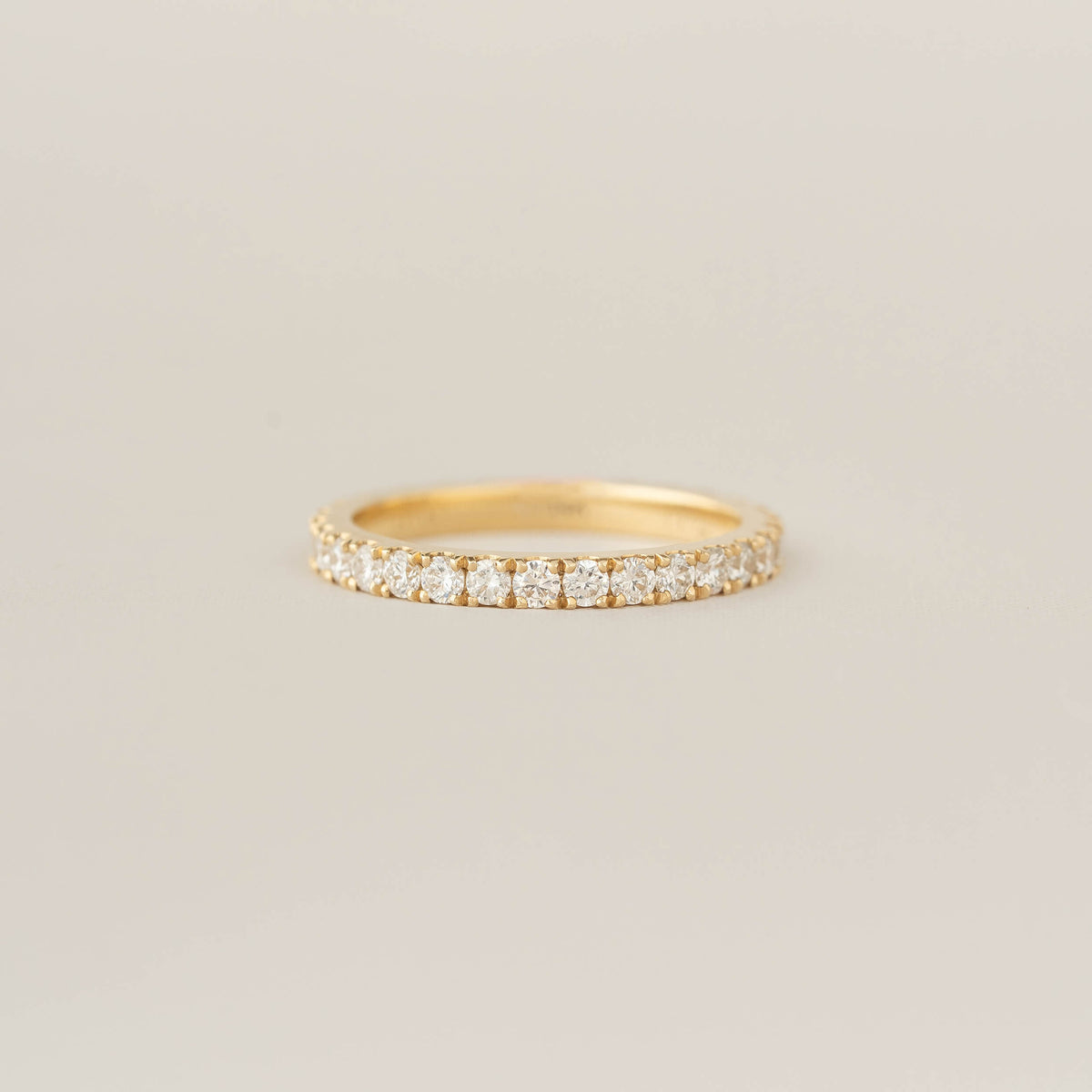 A delicate Gold band with a row of sparkling diamonds set around it, placed against a soft beige background, conveys elegance and simplicity.