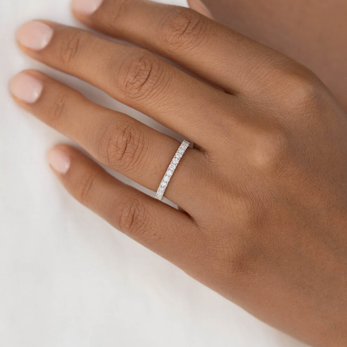 Close-up of a hand with a delicate White Gold diamond-studded ring on the ring finger. The skin tone is warm, and the nails are neatly manicured.