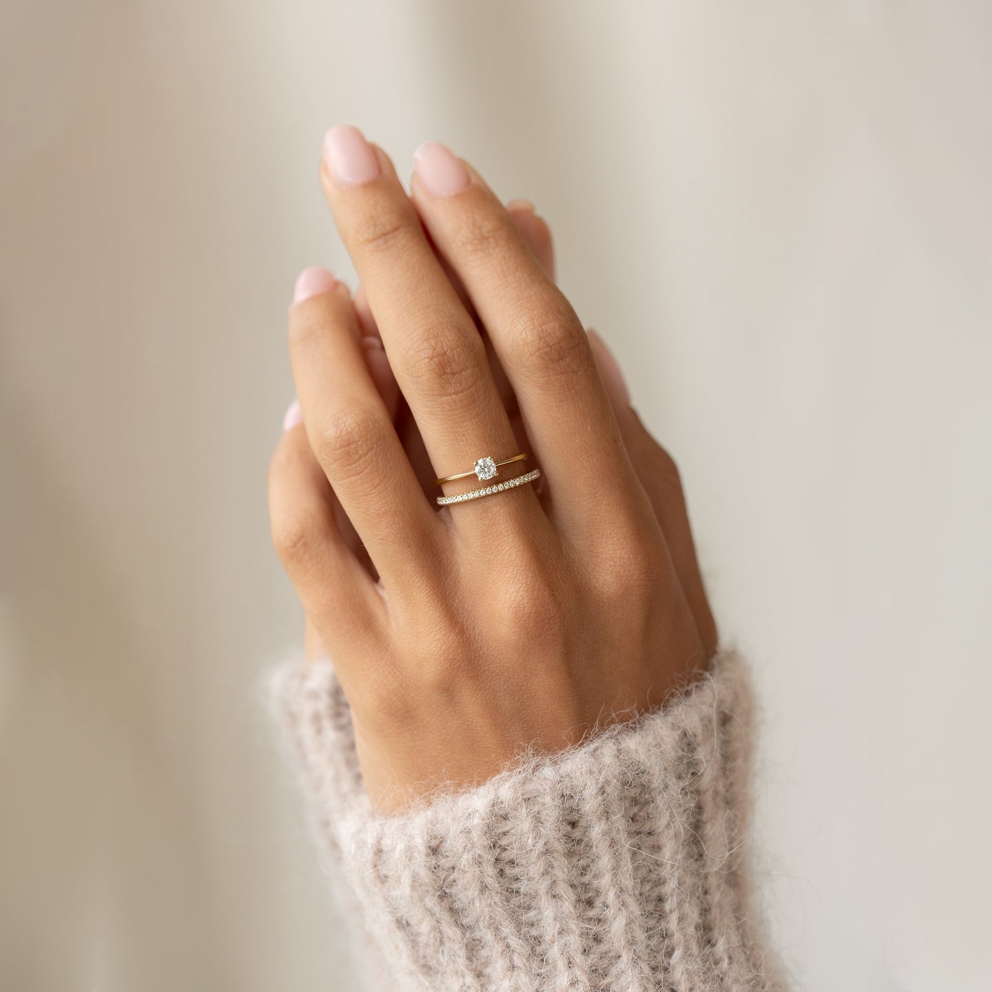 Close-up of a hand wearing a 14k gold Diamond Eternity Ring paired with a solitaire engagement ring on a neutral background