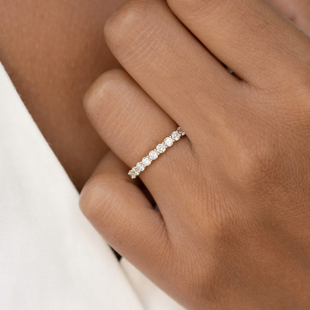 A close-up of a hand wearing an elegant Gold diamond eternity band with a series of sparkling stones set in a gold band, against a soft beige background.