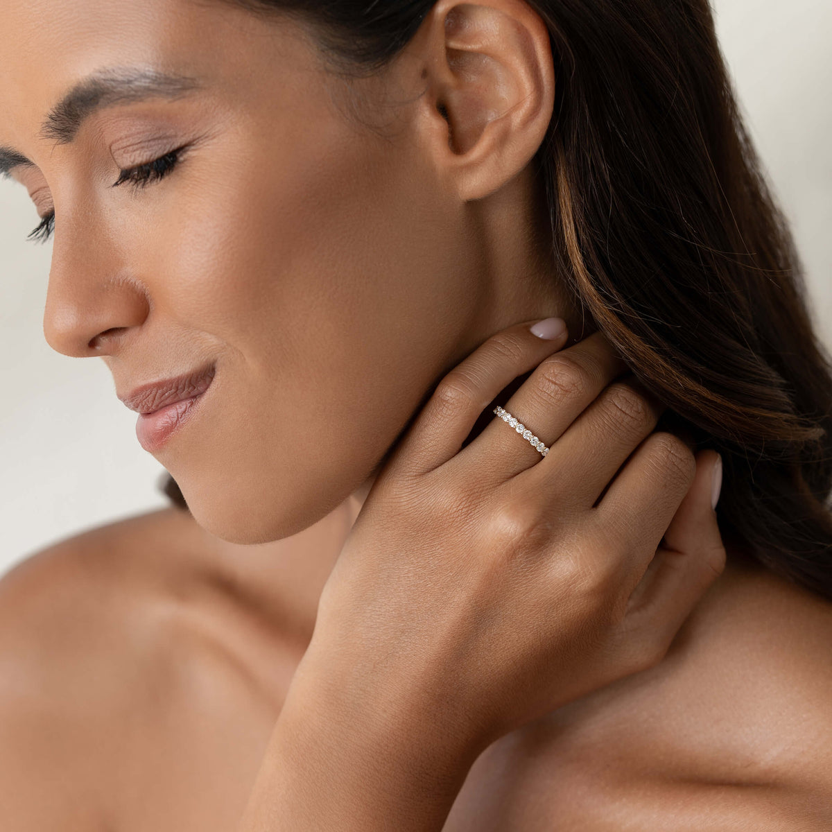 A woman with closed eyes and a serene expression gently touches her neck, showcasing a sparkling Gold diamond ring on her finger. The tone is calm and elegant.