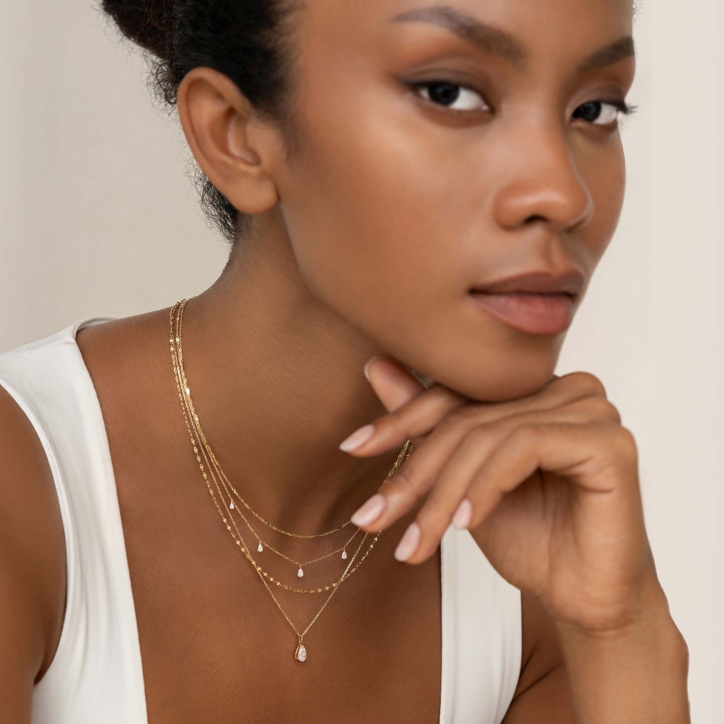 Close-up of a woman wearing Pear Cut Diamond Pendant Necklace 14k Gold - Sylvie with layered gold chains on neutral background