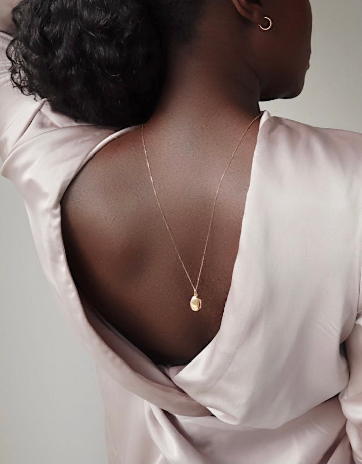 Close-up of a woman wearing a pale pink backless blouse and a delicate gold necklace with a small pendant