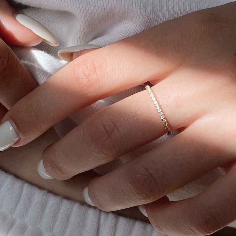 Close-up of a hand with natural nails wearing a delicate gold ring resting on white textured fabric in soft natural light