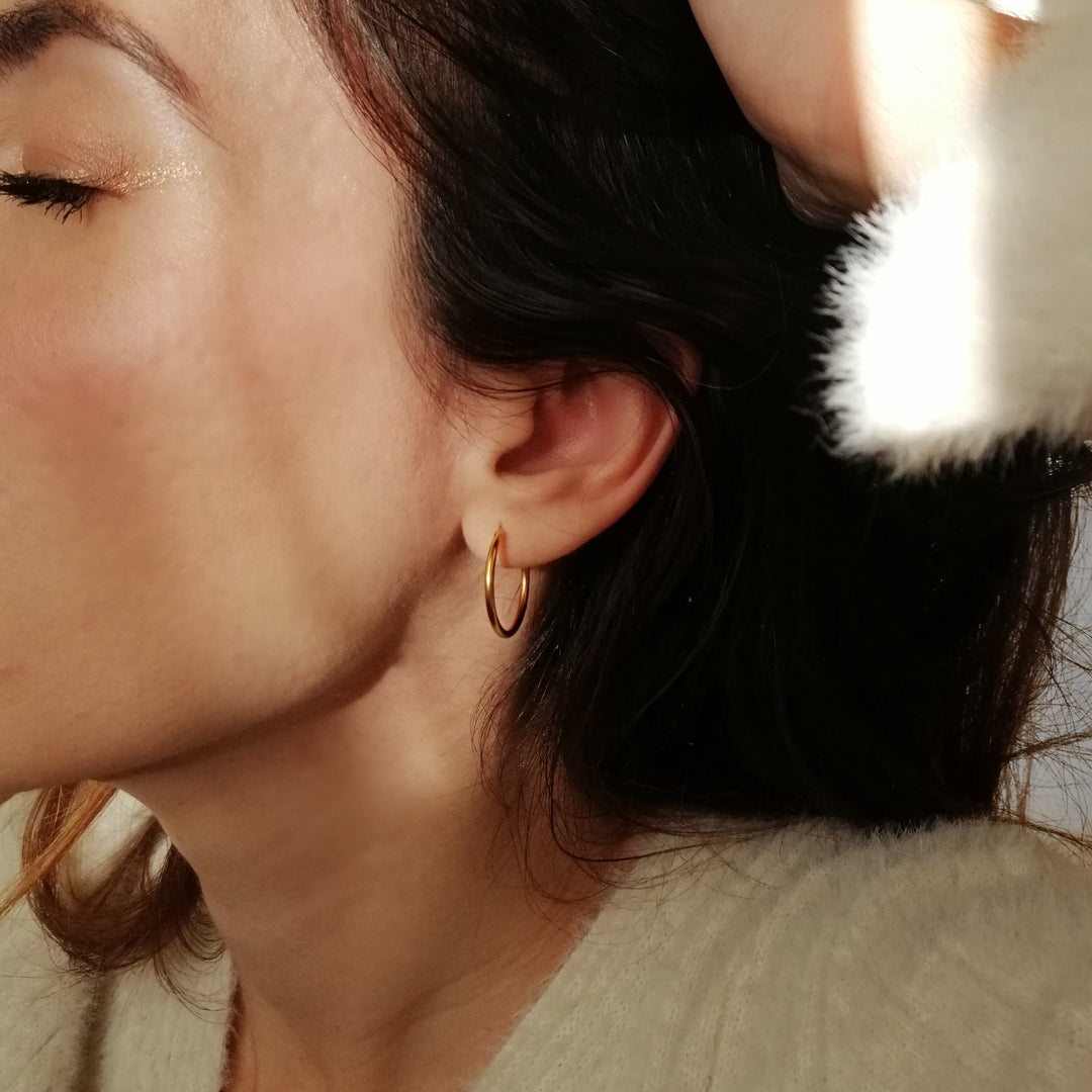 Close-up of a woman with dark hair wearing a small gold hoop earring and a cream sweater in soft natural light