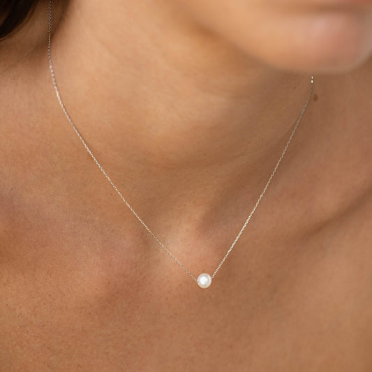 Close-up of a woman wearing the Floating Pearl Necklace White Gold - Caris with a single pearl on a delicate chain