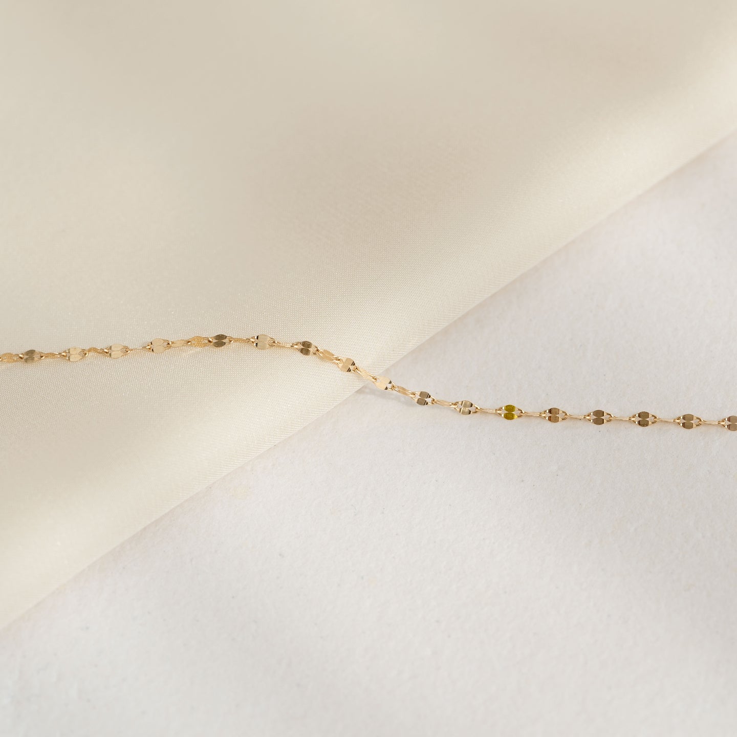 Close-up of Petal Chain Bracelet 14k Gold - Florence resting on a soft beige and white fabric background