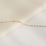 Close-up of Petal Chain Bracelet 14k Gold - Florence resting on a soft beige and white fabric background